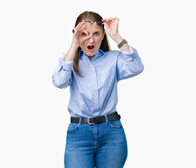 Beautiful middle age mature business woman wearing glasses over isolated background doing ok gesture shocked with surprised face, eye looking through fingers. Unbelieving expression.