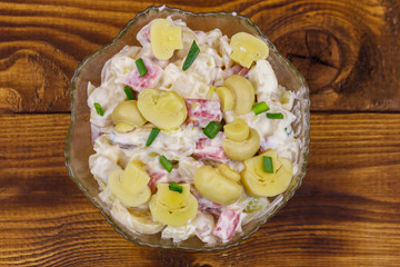 Potato salad with marinated mushrooms, sausage, onion and mayonnaise on wooden table