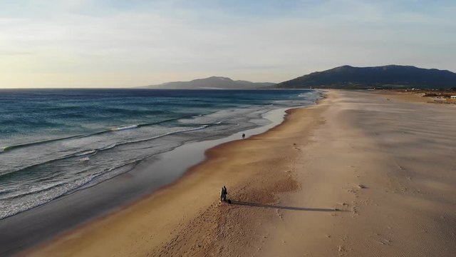 Atlantic coast beach is the city of Tarifa Spain, waves surf and sandy beach at sunset. Empty beach in winter, few people walking along the coast of Spain