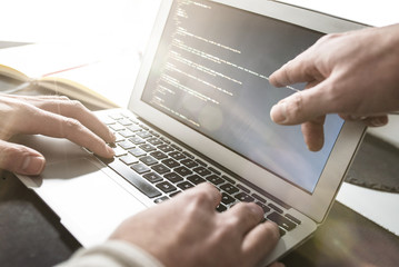 close-up of person working on laptop computer while other is pointing at monitor indicating something