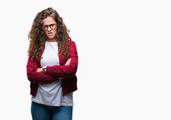 Beautiful brunette curly hair young girl wearing jacket and glasses over isolated background skeptic and nervous, disapproving expression on face with crossed arms. Negative person.