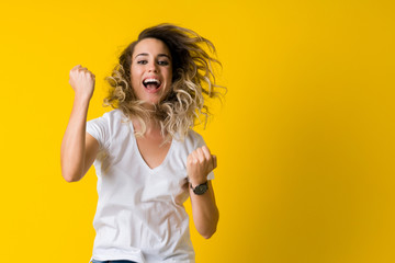 Beautiful young blonde woman jumping happy and celebrating with raised hands and open mouth over isolated yellow background