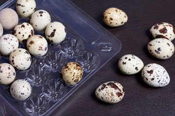 Quail eggs. They lie in a plastic container. Next on the table are a few eggs. On a dark background.