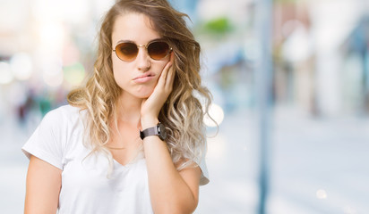 Fototapeta na wymiar Beautiful young blonde woman wearing sunglasses over isolated background thinking looking tired and bored with depression problems with crossed arms.