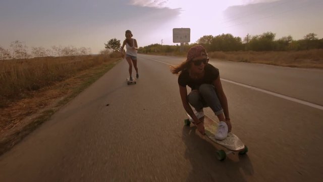 Two young fit women keeping balance while cruising on longboards during summer vacations in the countryside in Eastern Europe