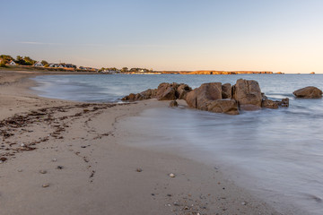 French landscape - Bretagne. A beautiful beach with rocks and port in the background at sunrise.