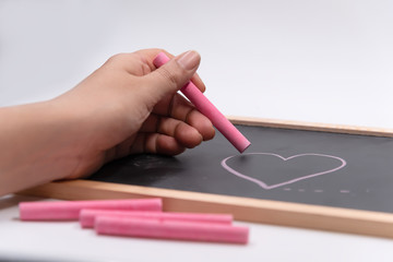 Hand hold color chalk draw cartoon heart shape on blackbroad.Tell love in valentine day or tell save good health and heart.