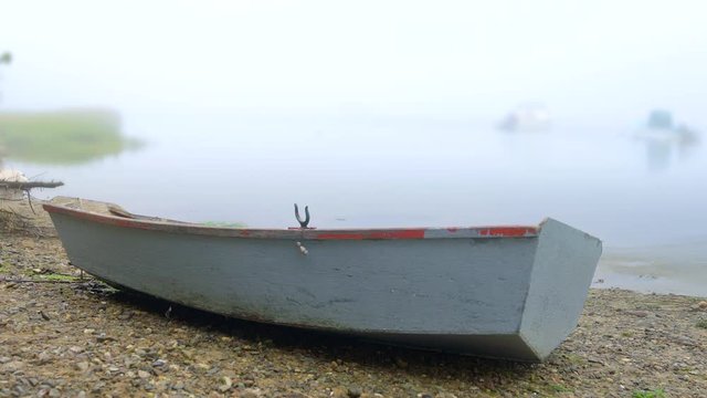 Rustic wooden rowboat dinghy beached on rocky shore. Camera pans right.