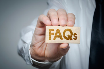 Businessman showing wooden block displaying FAQ word. Questions and answers concept.
