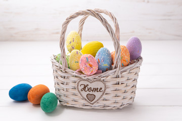 Easter eggs in a white basket on a white wooden background
