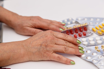 Concept for medicine. The hands of an elderly woman choose the right medicine among different drugs.