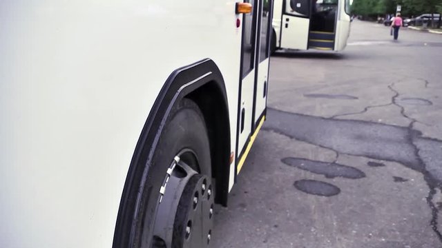 Side view of the white bus and bus wheel stopping on grey asphalt background. Scene. Close up of white passenger bus and its wheel, commercial transport wheels concept.