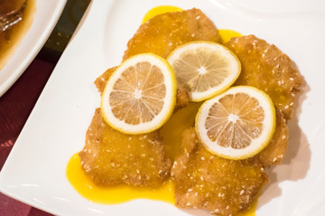 Close up view of lemon chicken with  sauce and slice lemons on top in white plate