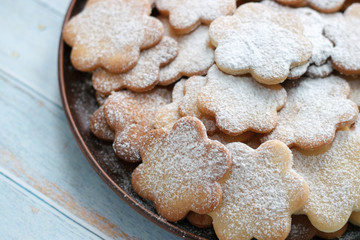 Original cookies biscuits sprinkled with powdered sugar on a plate of clay on a blue wooden background