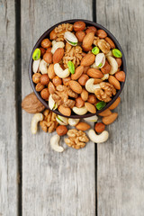 Wooden bowl with mixed nuts on a wooden gray background. Walnut, pistachios, almonds, hazelnuts and cashews, walnut.