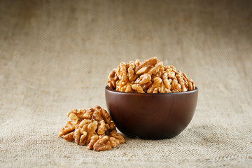 Peeled walnuts in a wooden, dark brown cup on a burlap cloth.