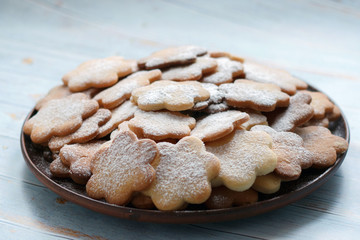 Original cookies biscuits sprinkled with powdered sugar on a plate of clay on a blue wooden background