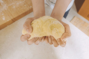 Woman hands hold prepared dough for pasta or bread on kitchen table.
