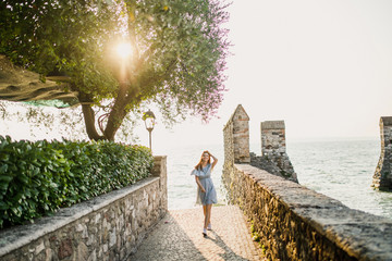 young beautiful girl with red hair in a blue dress walks at sunrise on the seashore