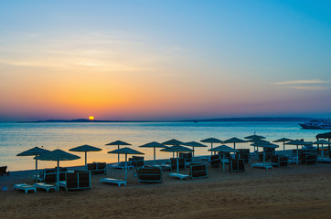 Sunrise, sunset on the beach with umbrellas orange and blue color at dusk.