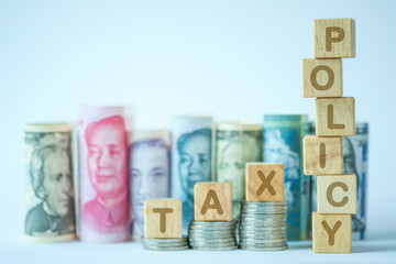 Tax policy keywords on wooden cubes stack on coins and variety banknote background such as Yuan US dollar.Tax policy in each countries concept.