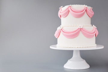 White wedding cake with pink elements made from pastry mastic on a gray background. Sugar flowers,...