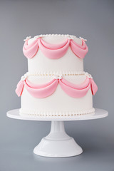 White wedding cake with pink elements made from pastry mastic on a gray background. Sugar flowers, marzipan flowers and mastic, beautiful decor for decorating cakes.