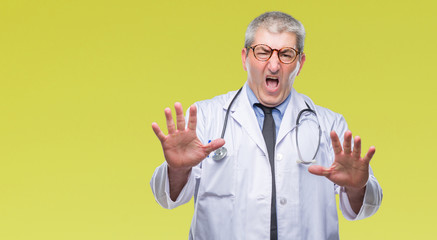 Handsome senior doctor man over isolated background afraid and terrified with fear expression stop gesture with hands, shouting in shock. Panic concept.