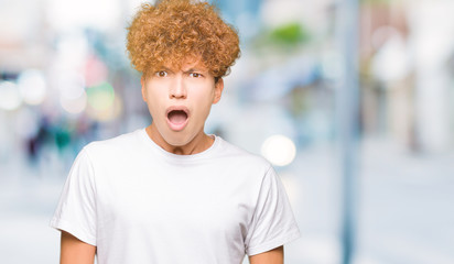 Young handsome man with afro hair wearing casual white t-shirt In shock face, looking skeptical and sarcastic, surprised with open mouth