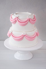 White wedding cake with pink elements made from pastry mastic on a wooden background. Sugar flowers, marzipan flowers and mastic, beautiful decor for decorating cakes.