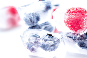 frozen blueberry and raspberry in ice cubes on white background