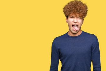 Young handsome man with afro hair sticking tongue out happy with funny expression. Emotion concept.