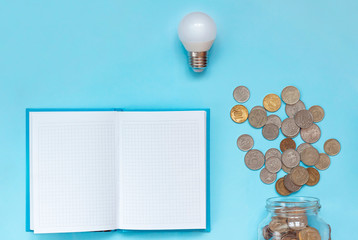 LED light bulb, coins and notepad on blue background. electricity metering concept. Power saving.