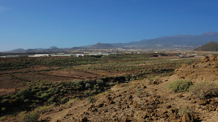 Fototapeta na wymiar Elevated views from Pelada Mountain, locally known as Montana Pelada towards the southern coast, highlighting scattered villages, the arid rocky soil and endemic flora, in Tenerife, Canary Islands, Sp