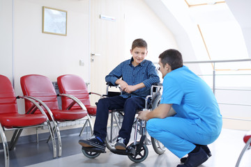 Fototapeta na wymiar Male doctor taking care of little boy in wheelchair indoors