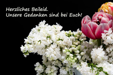 Weißer Flieder mit lila Tulpen vor schwarzem Hintergrund mit Kondulenztext