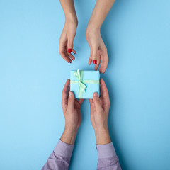 man gives a girl a gift from hand to hand,box wrapped in decorative paper with a bow background, the concept of holidays, love and relationships, top view