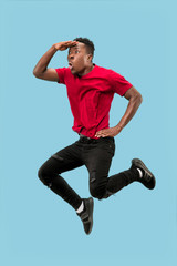 Freedom in moving and forward motion. The happy surprised young african man jumping a against blue studio background. Runnin man in motion or movement. Human emotions and facial expressions