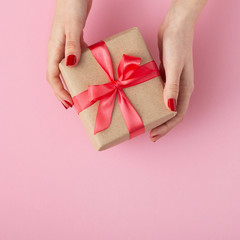girl holding a present in hands, women with gift box in hands wrapped in decorative paper on pink background, top view, concept holiday and gifts