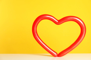 Heart figure made of modelling balloon on table against color background. Space for text