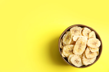 Wooden bowl with sweet banana slices on color background, top view with space for text. Dried fruit as healthy snack