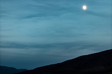 Bright moonlight over a blue dusk sky and mountain silhouette