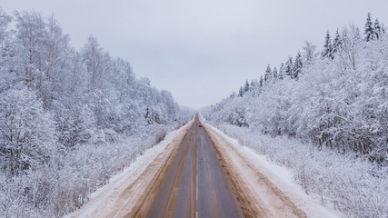 Aerial view of forest covered with snow, road in winter time