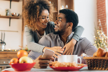 Loving young couple using smartphone in kitchen
