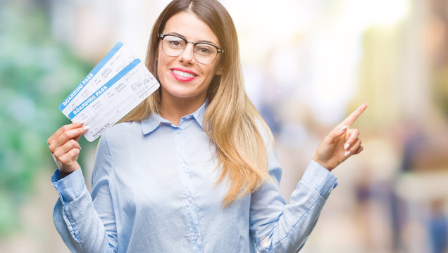 Young beautiful woman holding boarding pass over isolated background very happy pointing with hand and finger to the side
