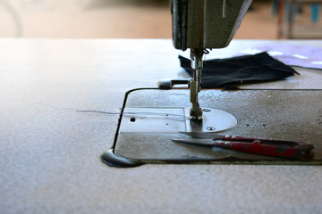 the old scissor ,blue thread in presser foot and black cloth on panel of old sewing machine  with bright light