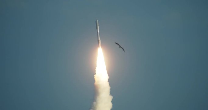 Amazing close-up shot of commercial Space Rocket lifting off with bright flames and exhaust smoke in front of dramatic sky.  Seagull flies through the shot. 4K at  120 fps slow motion.