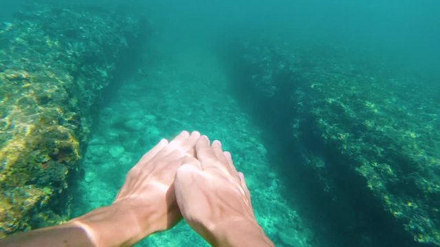 man swims underwater in oceaan among coral reefs. first person view