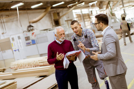 Three men standing and discuss in furniture factory
