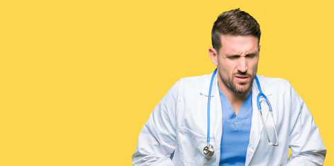 Handsome doctor man wearing medical uniform over isolated background with hand on stomach because nausea, painful disease feeling unwell. Ache concept.